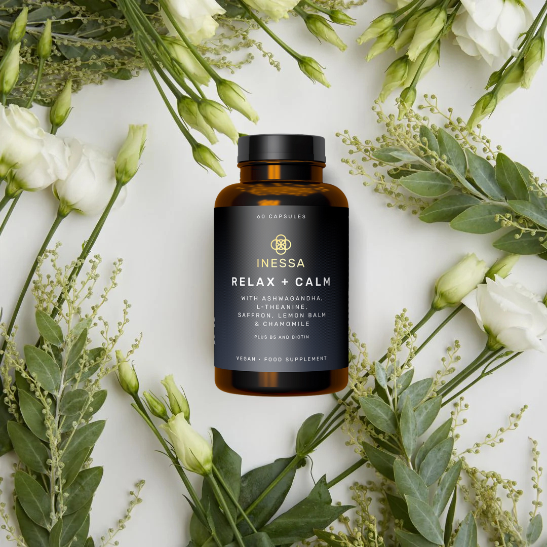 A bottle of dietary supplements surrounded by green foliage and white flowers.