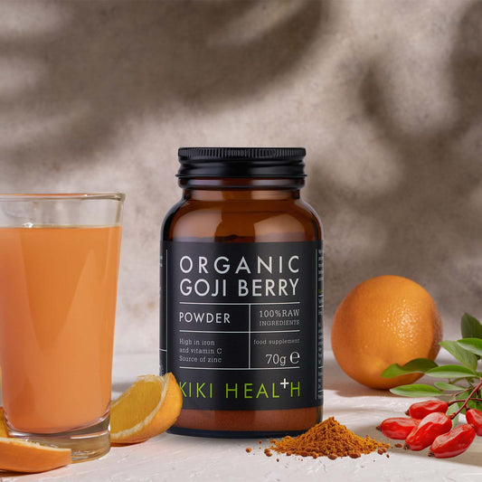 A bottle of organic goji berry powder with a glass of orange juice, fresh orange, and goji berries.