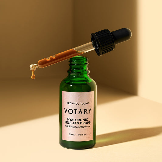 A green glass bottle with a dropper releasing orange oil.