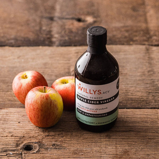 A bottle of organic apple cider vinegar next to three red apples.