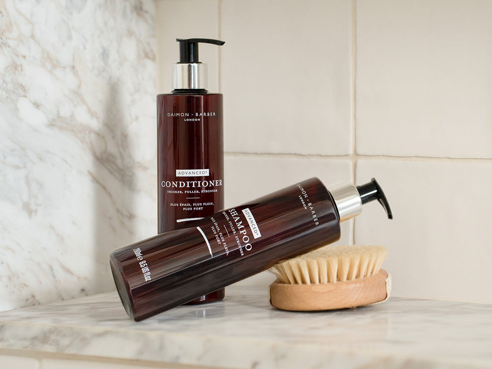 Two bottles of shampoo and conditioner with a brush on a marble surface.