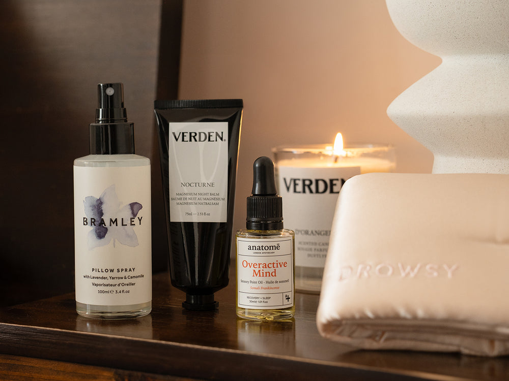 Bath and body products including a pillow spray, lotion, and candles on a wooden surface.